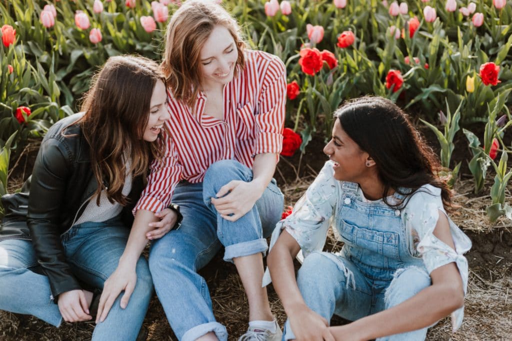 3 girlfriends sitting in flower field laughing