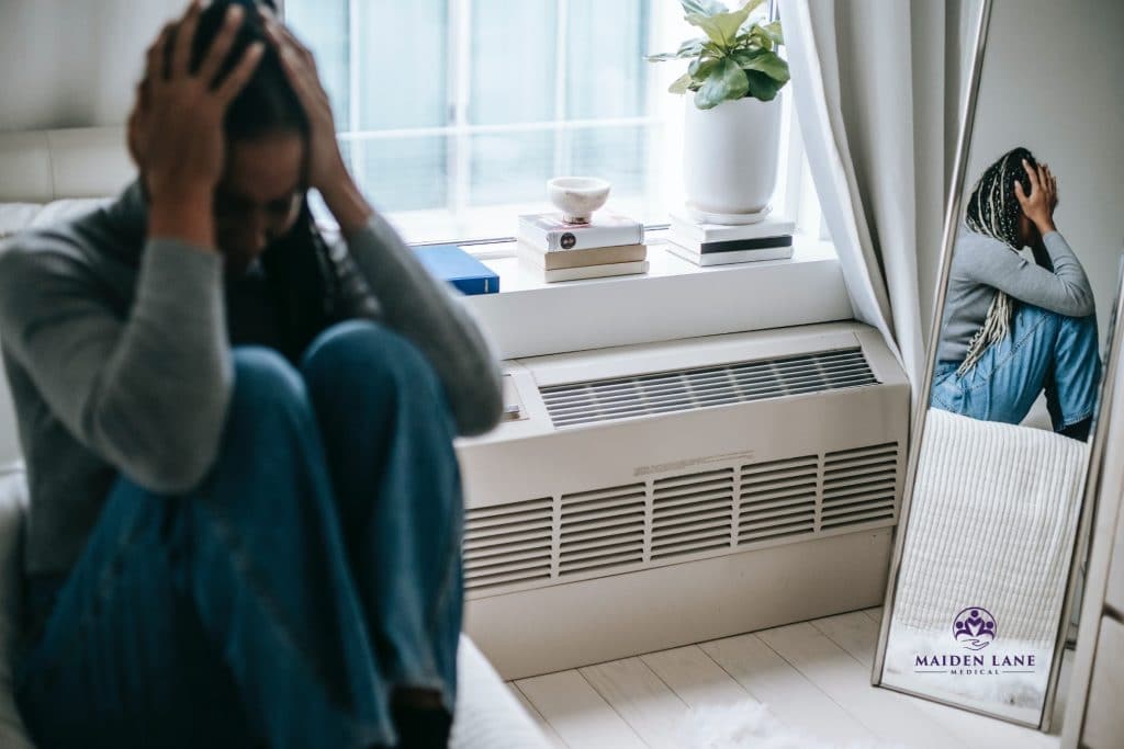 Young african american woman sitting on her bed depressed about a miscarriage. - Maiden Lane Medical | New York, NY