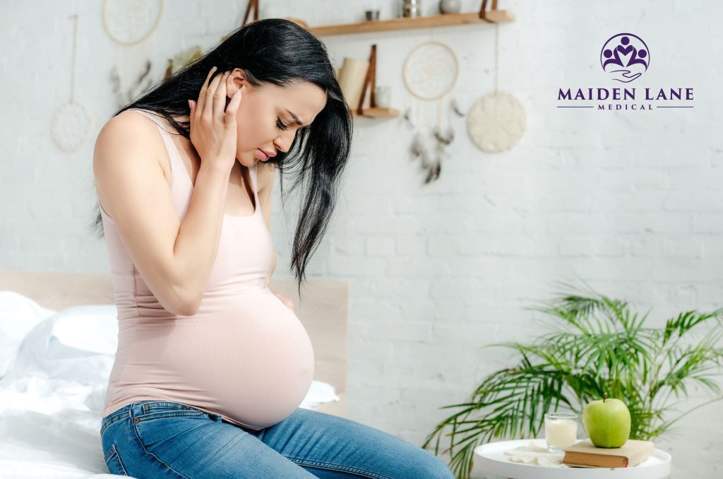 A pregnant woman looking down at belly with a worried look.