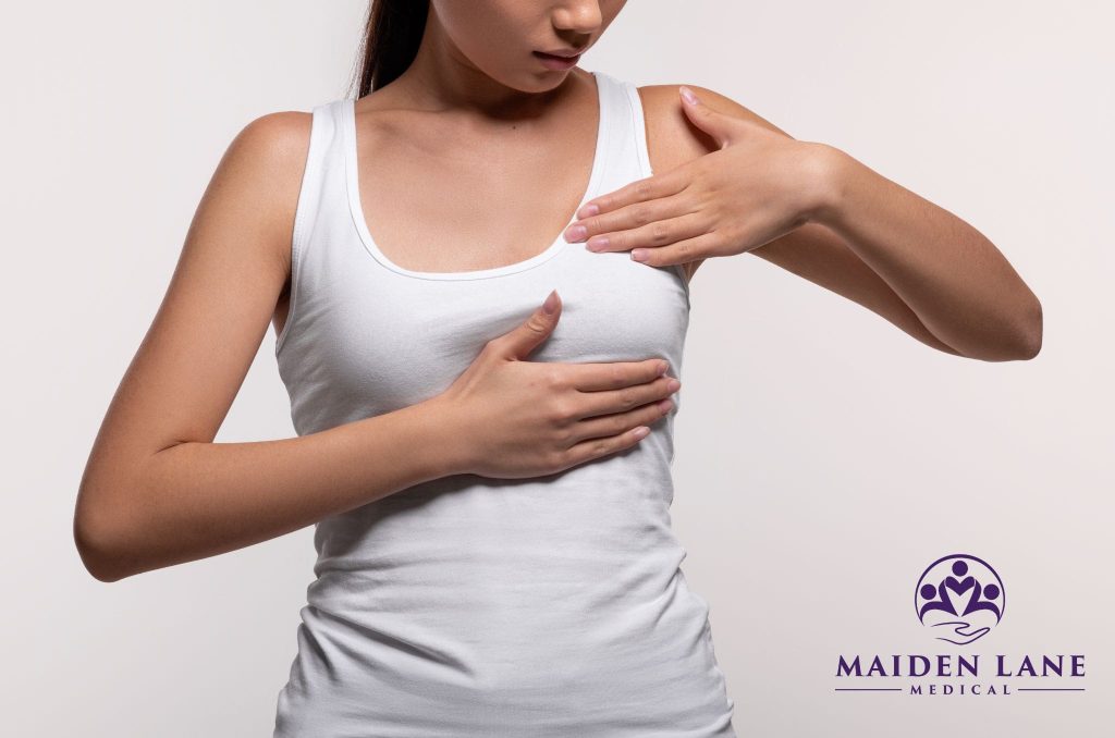 A woman examining her breast with her hands over her shirt before a mammogram.