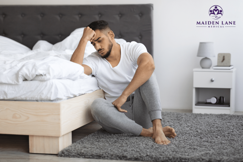 A man sitting next to a bed disappointed because he has premature ejaculation issues in Manhattan, New York.